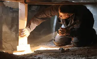 A professional inspecting wooden beams under the floor of a structure in Albuquerque, NM